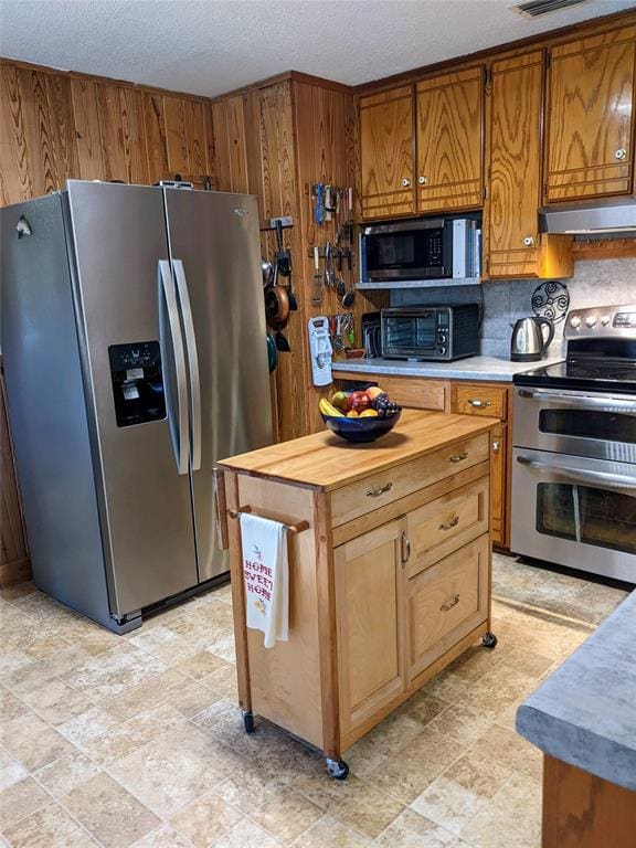 kitchen with appliances with stainless steel finishes, a textured ceiling, tasteful backsplash, and wooden walls