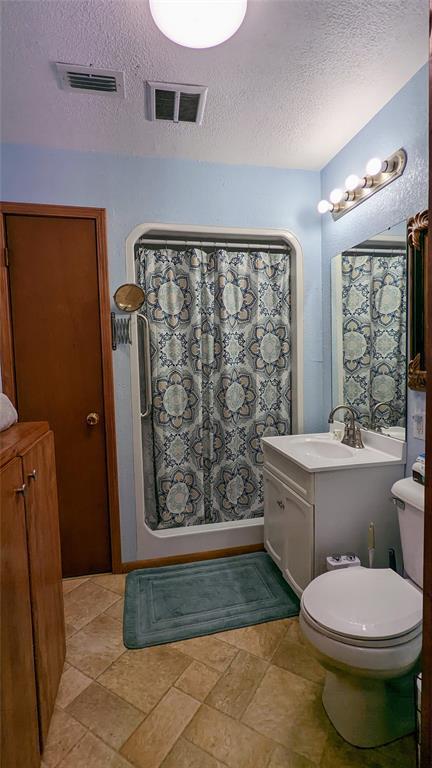 bathroom featuring a shower with shower curtain, vanity, toilet, and a textured ceiling