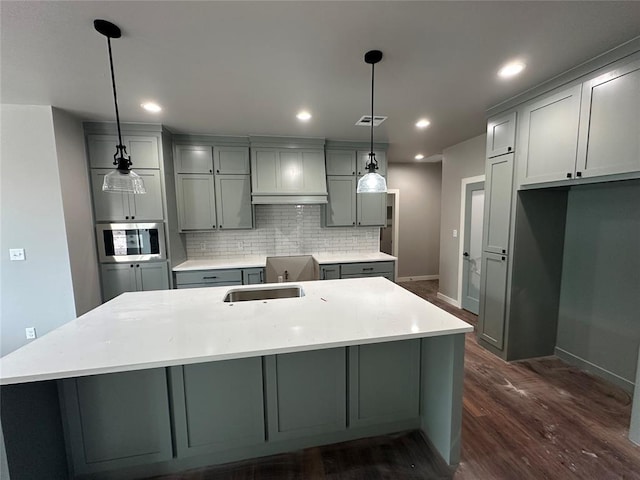 kitchen featuring backsplash, hanging light fixtures, gray cabinets, and a center island with sink