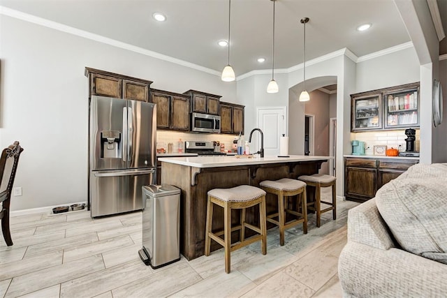 kitchen with appliances with stainless steel finishes, backsplash, a kitchen island with sink, crown molding, and decorative light fixtures