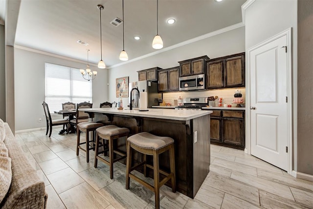 kitchen featuring backsplash, dark brown cabinets, stainless steel appliances, decorative light fixtures, and a center island with sink