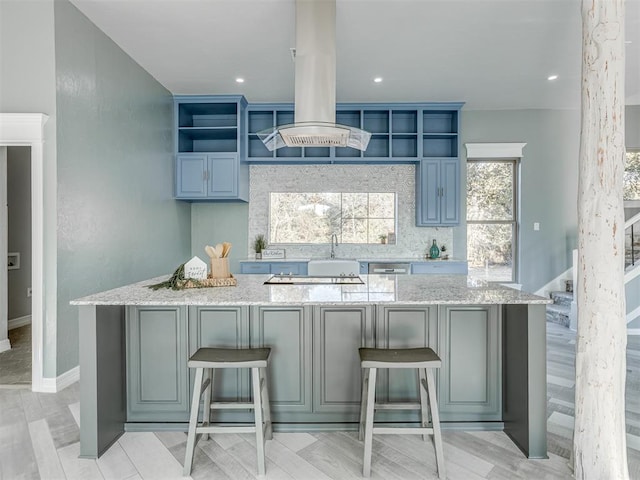 kitchen featuring a center island, light stone counters, a breakfast bar area, island range hood, and light wood-type flooring