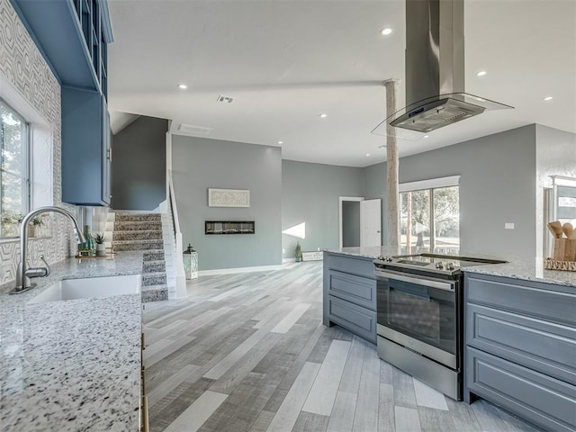 kitchen featuring light stone countertops, island range hood, sink, electric stove, and light hardwood / wood-style flooring