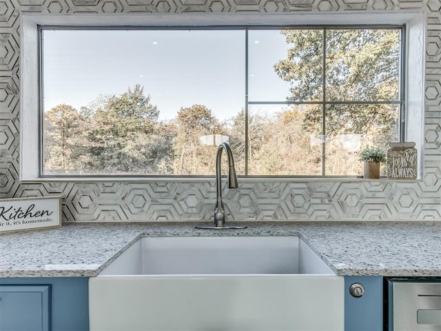 kitchen with blue cabinets, light stone counters, a wealth of natural light, and sink