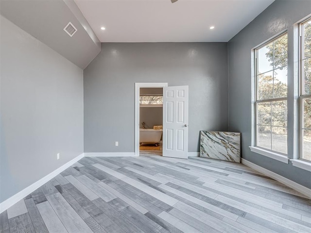 spare room featuring a healthy amount of sunlight, lofted ceiling, and light hardwood / wood-style flooring