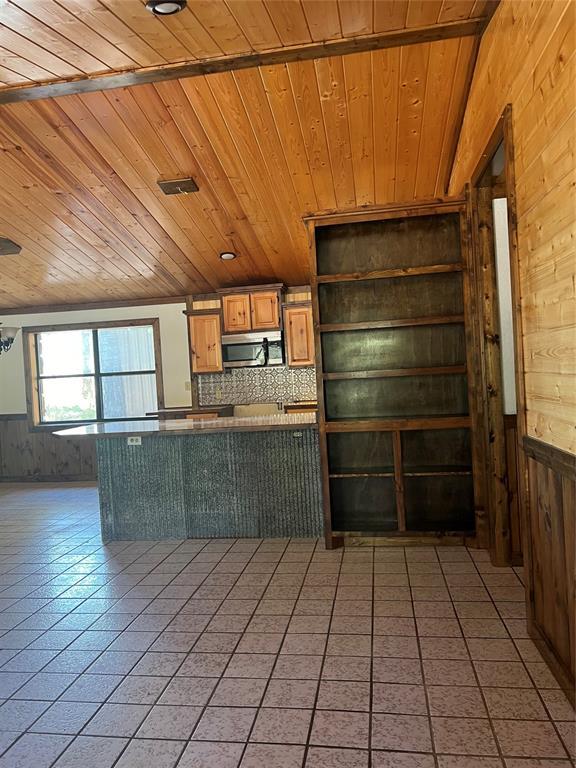 kitchen featuring wood walls, wood ceiling, light tile patterned floors, kitchen peninsula, and backsplash