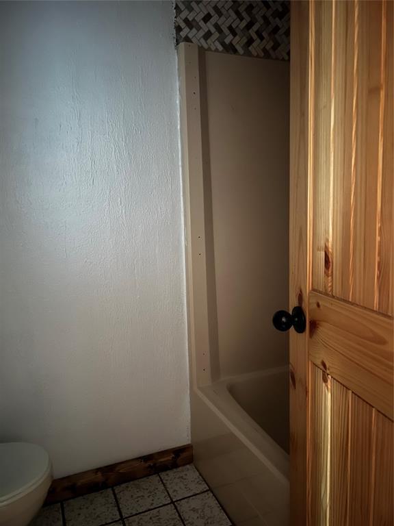 bathroom with tile patterned flooring, a tub, and toilet