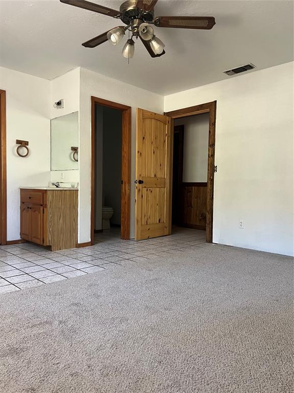 unfurnished bedroom featuring connected bathroom, light colored carpet, and ceiling fan