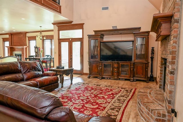 living room featuring french doors, a notable chandelier, crown molding, light hardwood / wood-style floors, and a fireplace