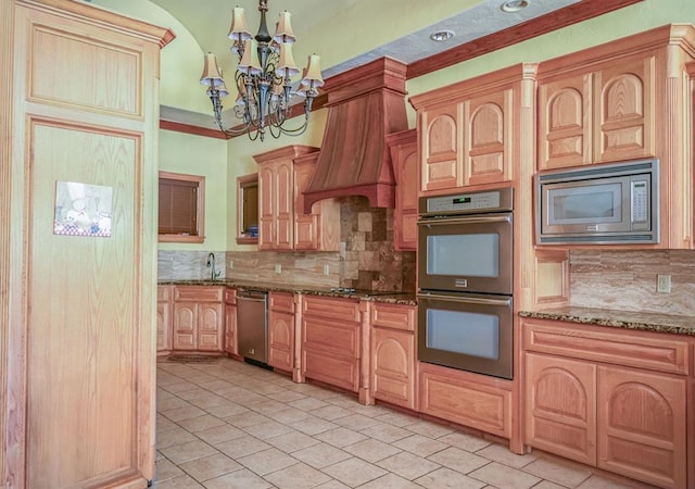 kitchen with appliances with stainless steel finishes, an inviting chandelier, custom range hood, and dark stone counters