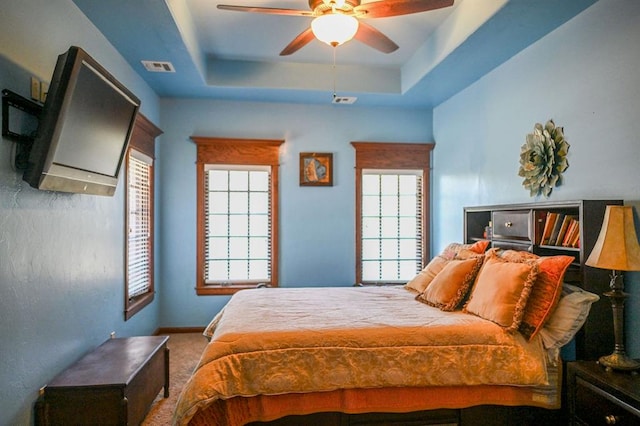 carpeted bedroom featuring a tray ceiling and ceiling fan