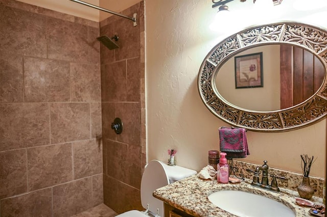 bathroom with tiled shower, vanity, and toilet