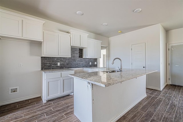 kitchen with white cabinetry, a kitchen island with sink, sink, and dark wood-type flooring