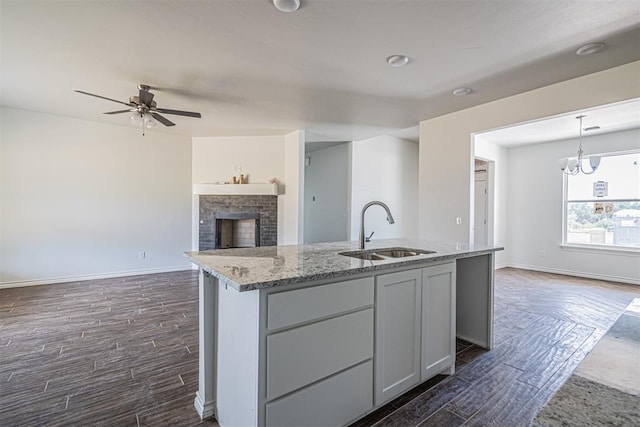 kitchen featuring pendant lighting, dark wood-type flooring, sink, a brick fireplace, and light stone countertops