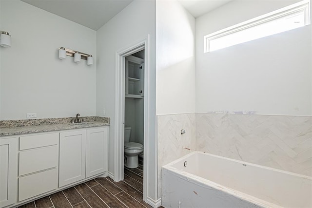 bathroom featuring wood-type flooring, vanity, a tub to relax in, and toilet