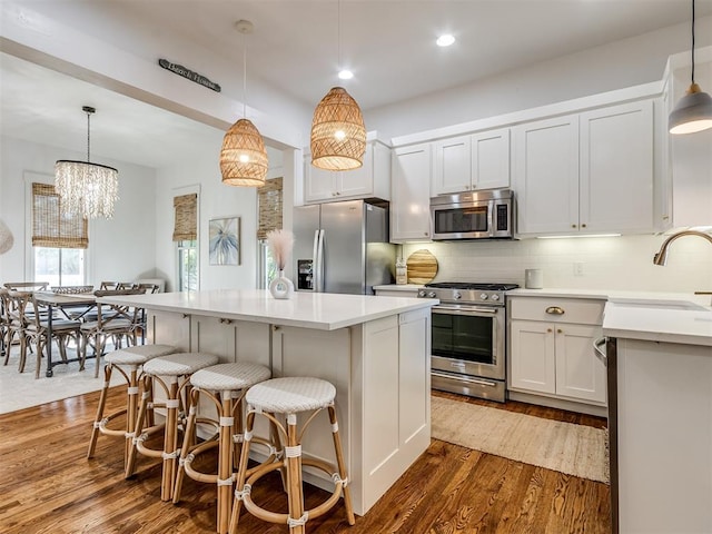 kitchen featuring dark wood-type flooring, hanging light fixtures, sink, appliances with stainless steel finishes, and a kitchen island