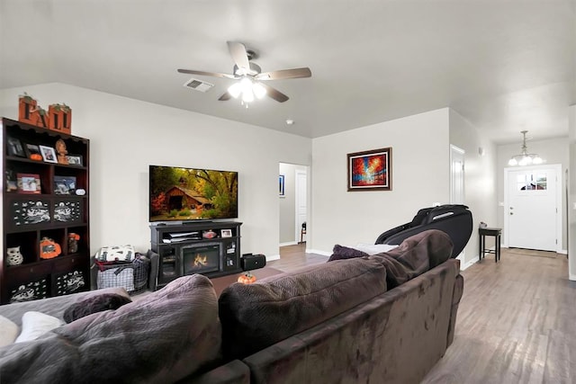 living room with visible vents, a glass covered fireplace, wood finished floors, baseboards, and ceiling fan with notable chandelier