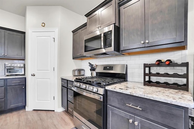 kitchen with light wood-style flooring, appliances with stainless steel finishes, decorative backsplash, and light stone counters