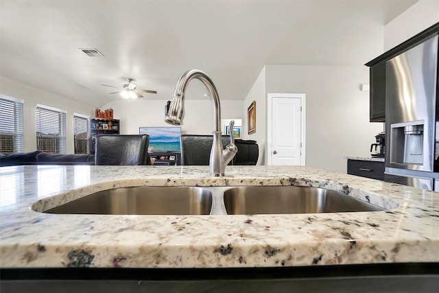 kitchen featuring light stone counters, lofted ceiling, a ceiling fan, open floor plan, and dark cabinets