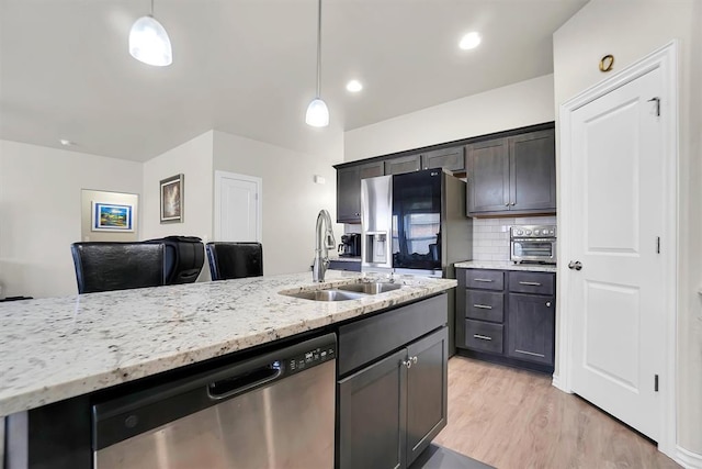 kitchen with a sink, hanging light fixtures, appliances with stainless steel finishes, light wood-type flooring, and tasteful backsplash