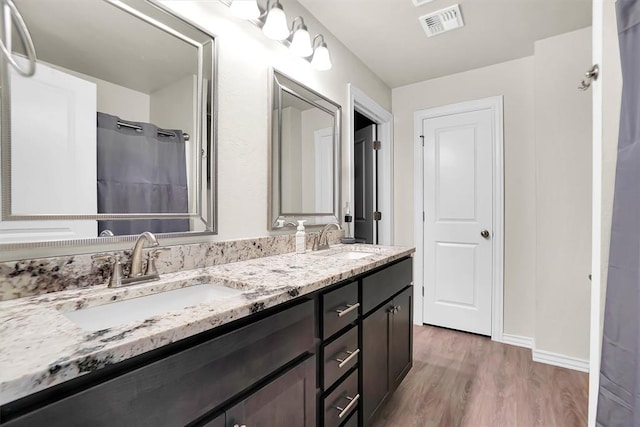 bathroom with double vanity, wood finished floors, a sink, and visible vents