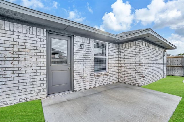 entrance to property featuring brick siding, a yard, fence, and a patio