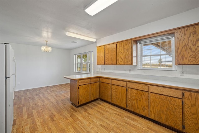 kitchen featuring pendant lighting, light hardwood / wood-style flooring, decorative backsplash, kitchen peninsula, and stainless steel refrigerator