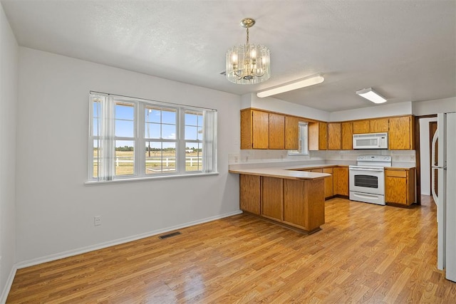 kitchen featuring light hardwood / wood-style floors, white appliances, kitchen peninsula, and hanging light fixtures