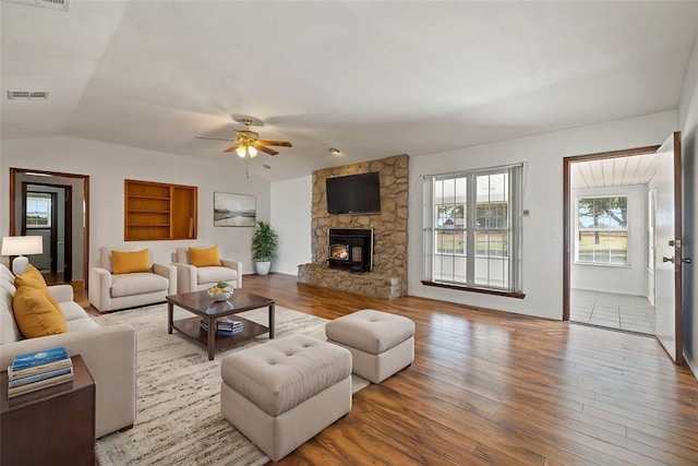 living room featuring vaulted ceiling, ceiling fan, hardwood / wood-style flooring, built in features, and a wood stove