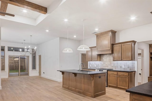 kitchen featuring sink, custom exhaust hood, hanging light fixtures, a kitchen island with sink, and stainless steel range with gas stovetop