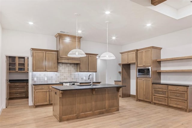 kitchen featuring sink, a kitchen island with sink, hanging light fixtures, stainless steel microwave, and tasteful backsplash