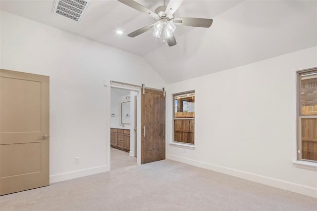 unfurnished bedroom with ensuite bath, ceiling fan, vaulted ceiling, light colored carpet, and a barn door