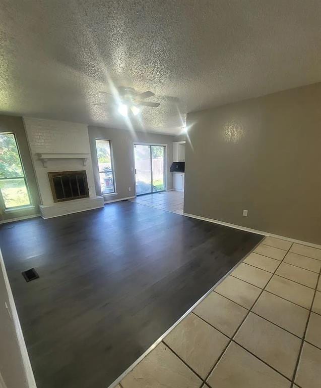 unfurnished living room featuring ceiling fan, a fireplace, a textured ceiling, and tile patterned flooring