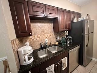 kitchen featuring backsplash, sink, dark stone countertops, light tile patterned floors, and stainless steel appliances