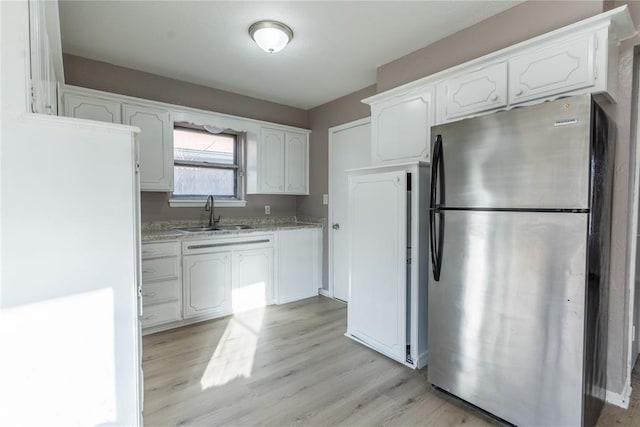 kitchen featuring sink, stainless steel fridge, light stone counters, white cabinets, and light wood-type flooring