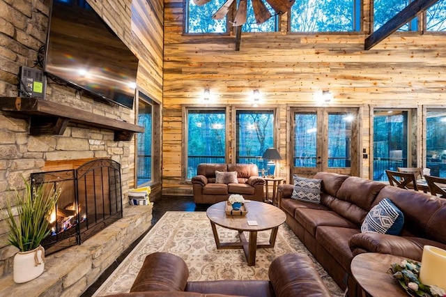 living room with a fireplace, ceiling fan, a towering ceiling, and wood walls