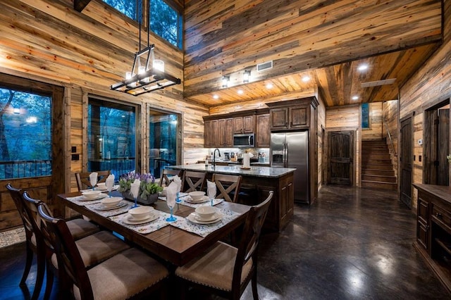 dining area with wooden ceiling, a towering ceiling, and wooden walls