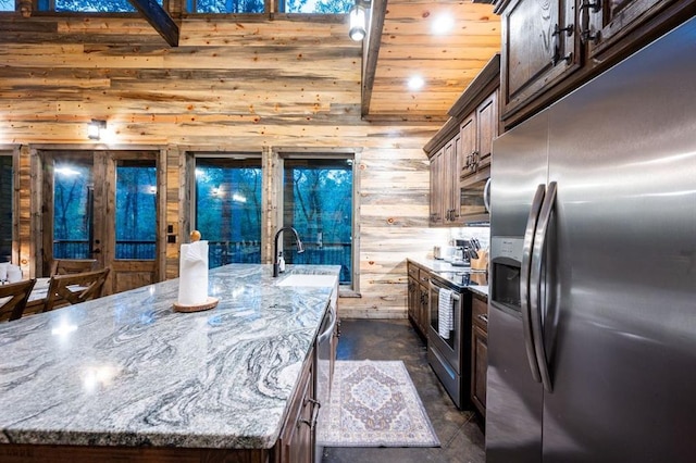 kitchen with a spacious island, sink, wooden walls, appliances with stainless steel finishes, and light stone counters