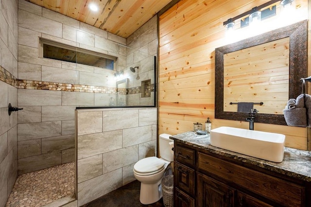 bathroom featuring vanity, wooden walls, toilet, wooden ceiling, and tiled shower