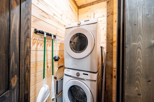 washroom featuring stacked washer and clothes dryer and wooden walls