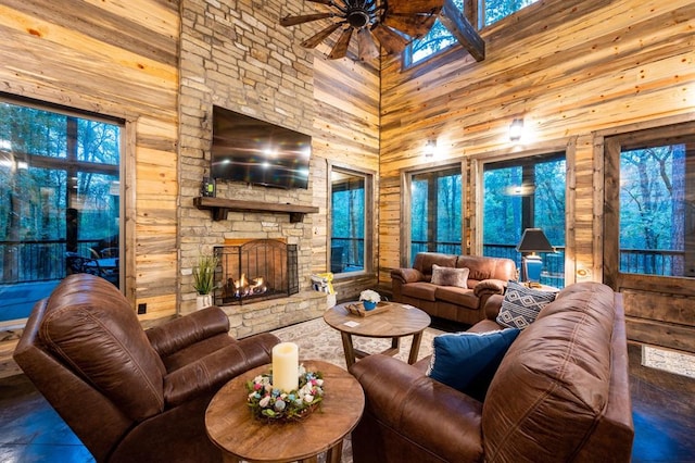 tiled living room featuring ceiling fan, a stone fireplace, wooden walls, and a high ceiling