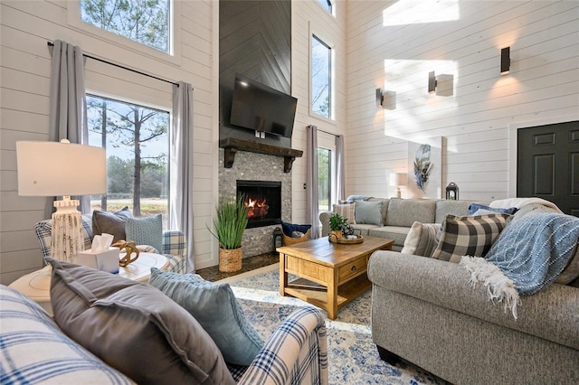 living room featuring a wealth of natural light, wood walls, a stone fireplace, and a high ceiling