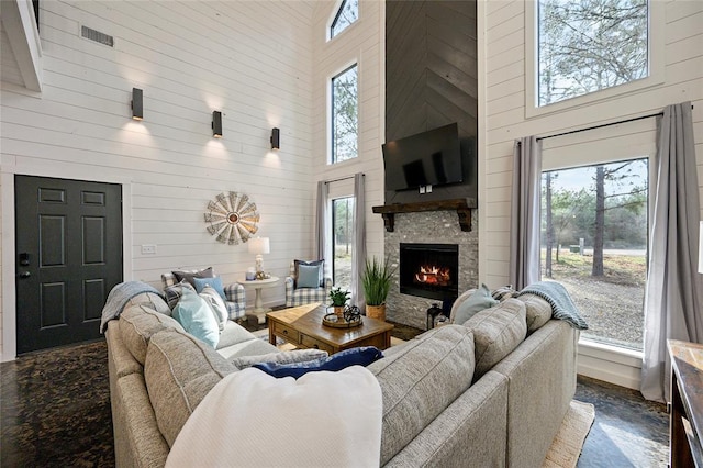 living room with plenty of natural light, wood walls, a stone fireplace, and high vaulted ceiling