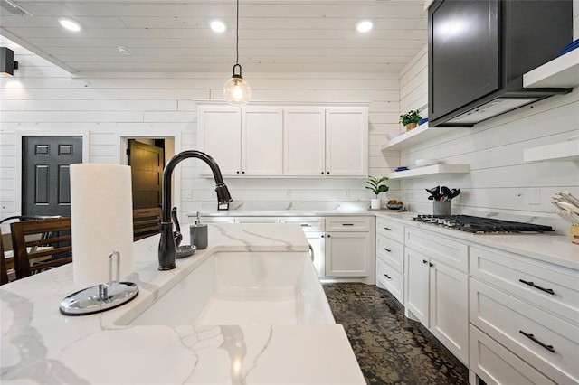 kitchen featuring light stone countertops, pendant lighting, white cabinetry, and wooden walls