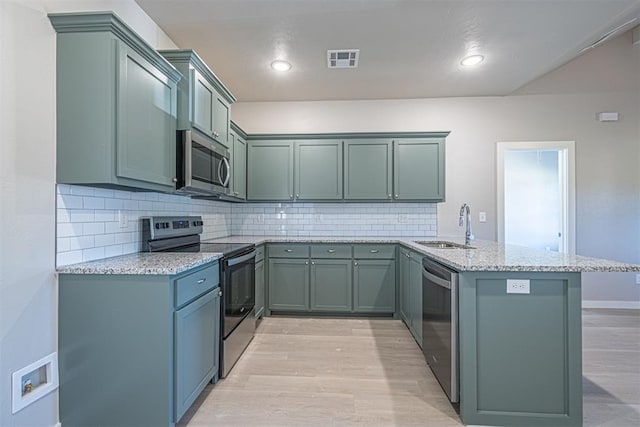 kitchen featuring kitchen peninsula, appliances with stainless steel finishes, light stone countertops, sink, and light hardwood / wood-style flooring