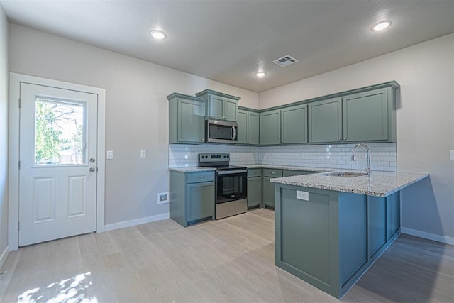 kitchen featuring tasteful backsplash, light stone counters, stainless steel appliances, sink, and light hardwood / wood-style flooring