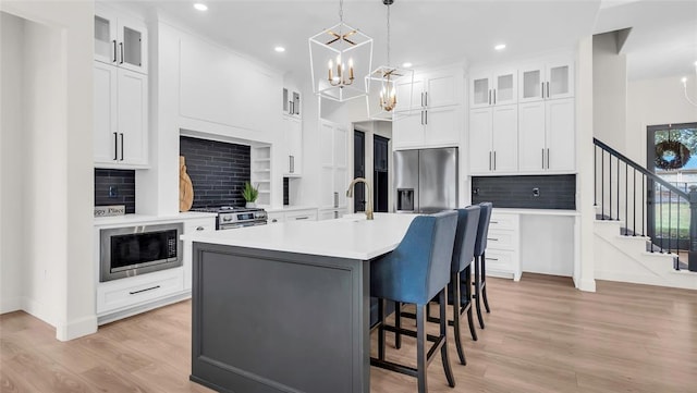 kitchen featuring appliances with stainless steel finishes, tasteful backsplash, white cabinetry, and an island with sink