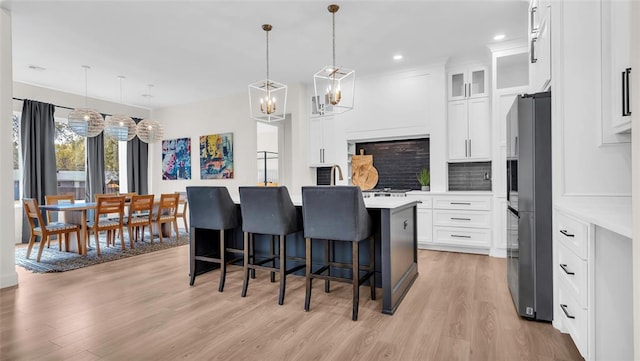 kitchen with stainless steel fridge, white cabinets, pendant lighting, and light wood-type flooring