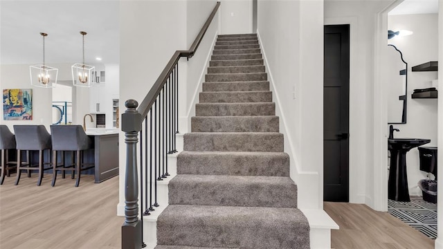 staircase with hardwood / wood-style floors, a notable chandelier, and sink