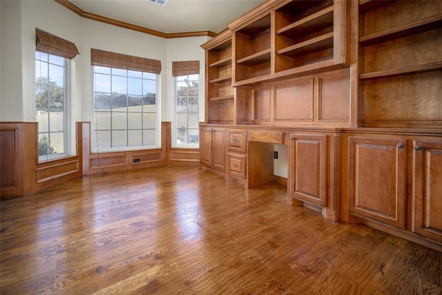 unfurnished office with hardwood / wood-style floors, built in desk, and crown molding